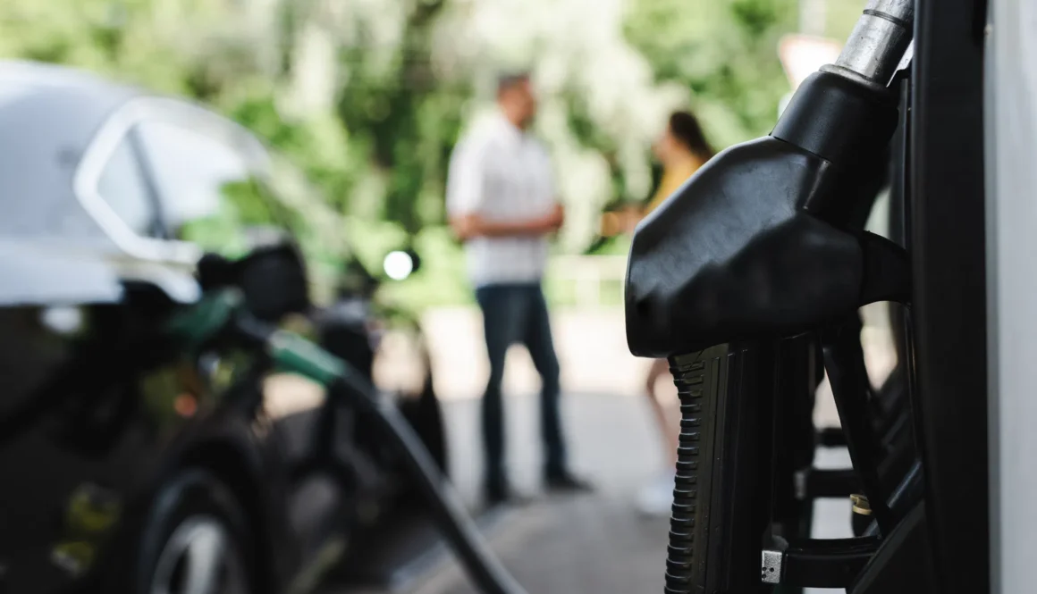Selective focus of fueling nozzle on gas station and couple standing near auto outdoors
