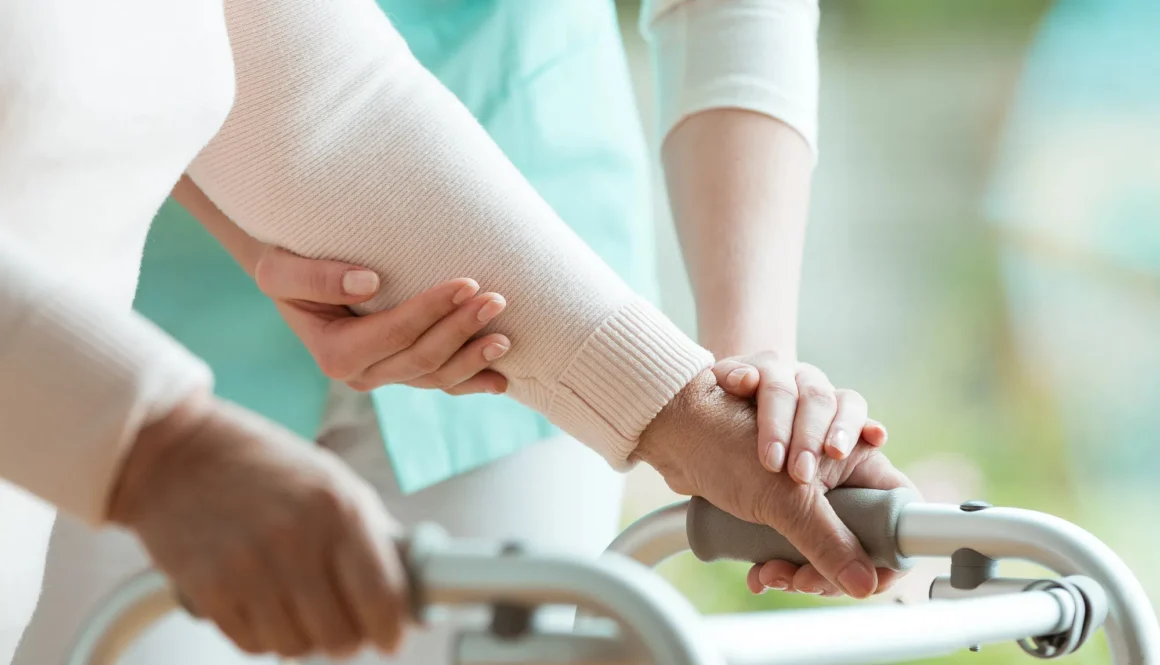 Closeup of senior lady's hands holding a walker and helpful nurse supporting her