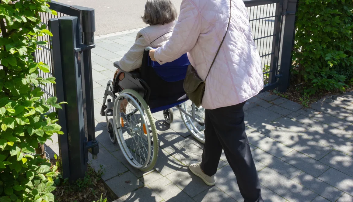 Senior lady walking and helping woman in wheelchair, Germany.
