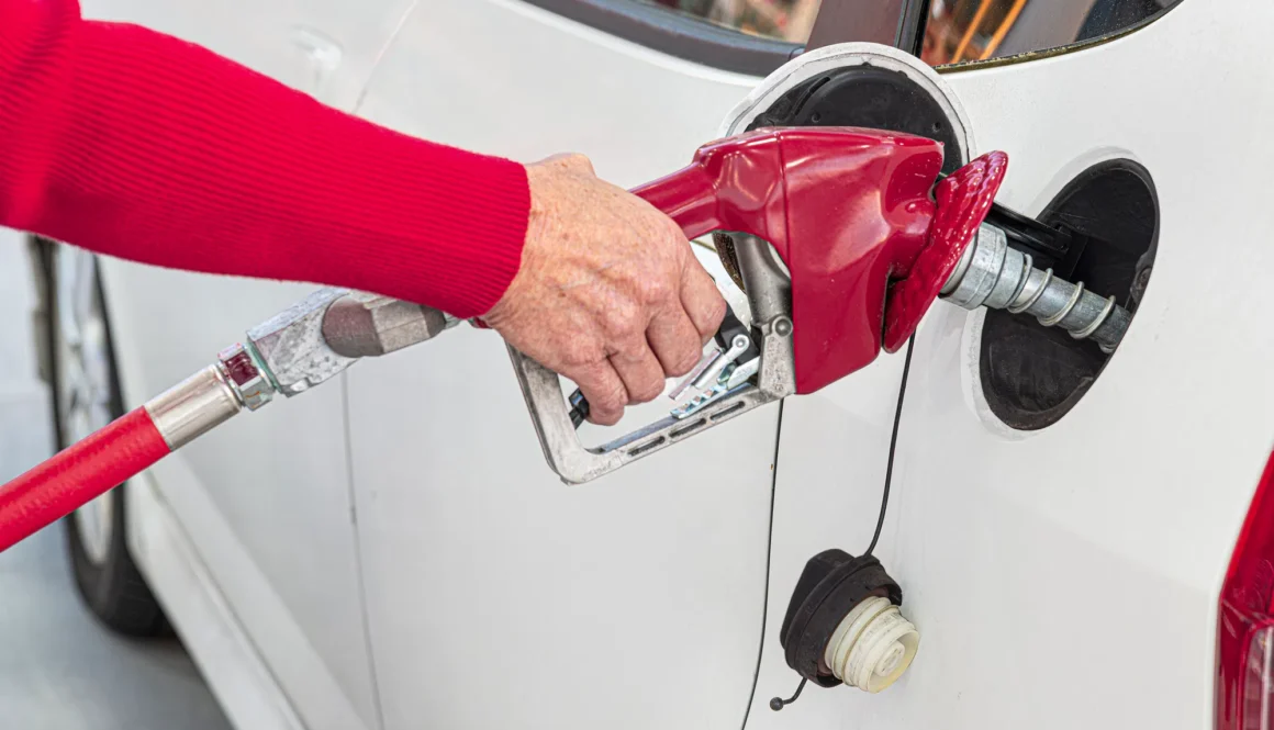 Horizontal close-up shot of a woman's hand pumping gas into her white car.