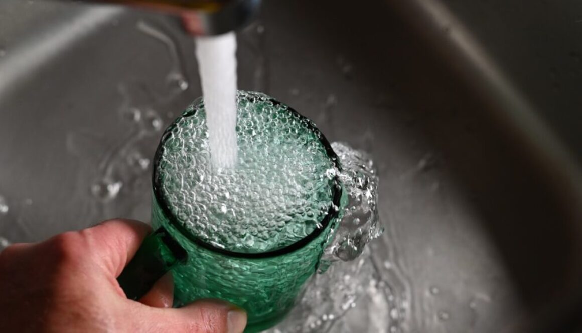 a person's hand is holding a green cup with water coming out of it
