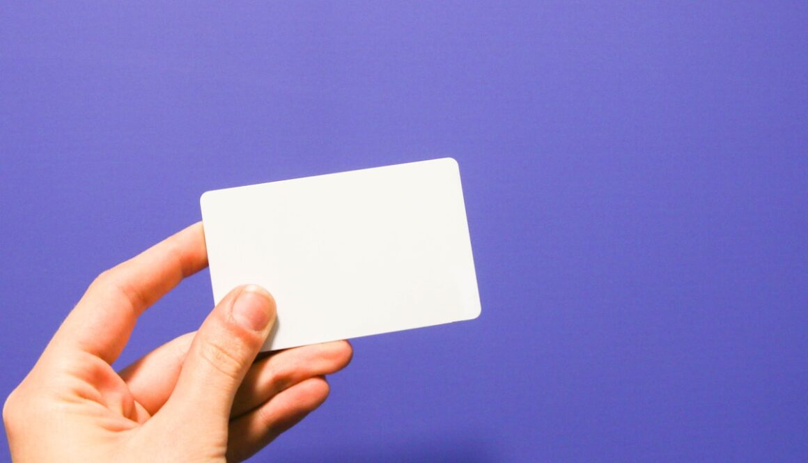 a hand holding a white business card against a purple background