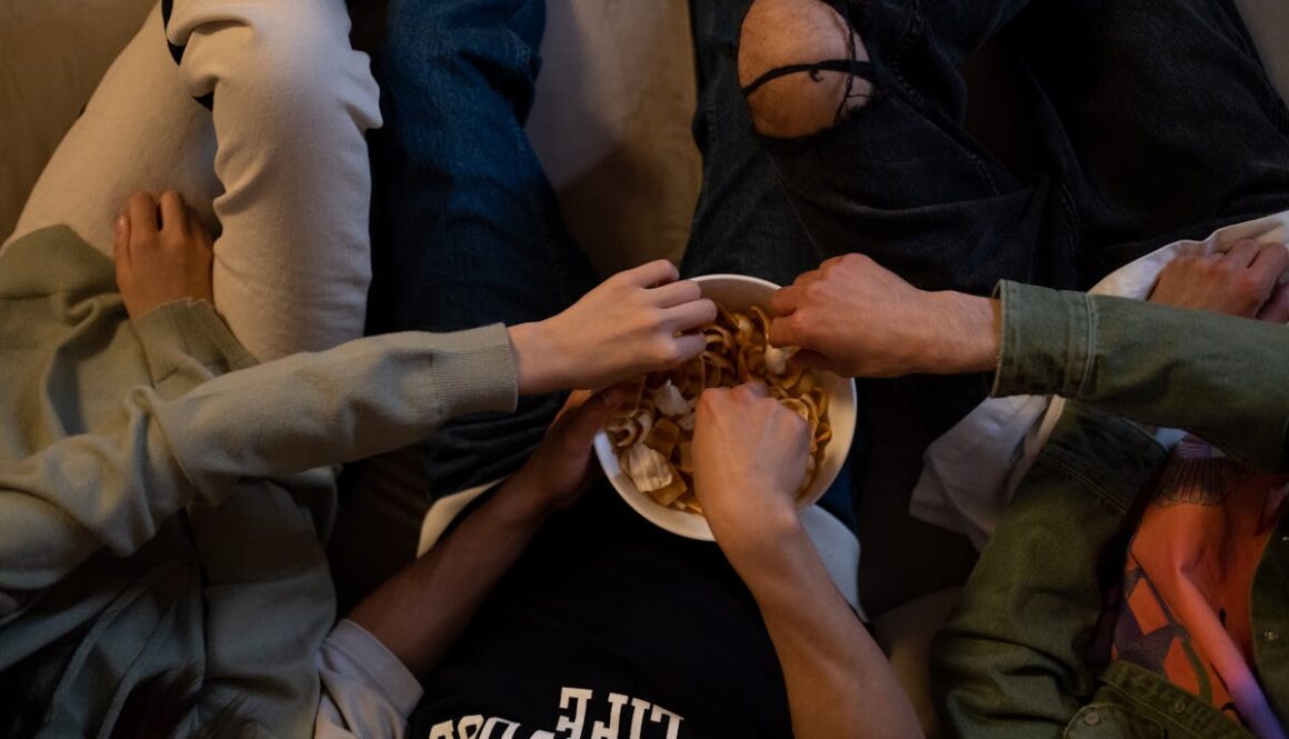 Close-up of friends reaching for snacks during a cozy movie night indoors.