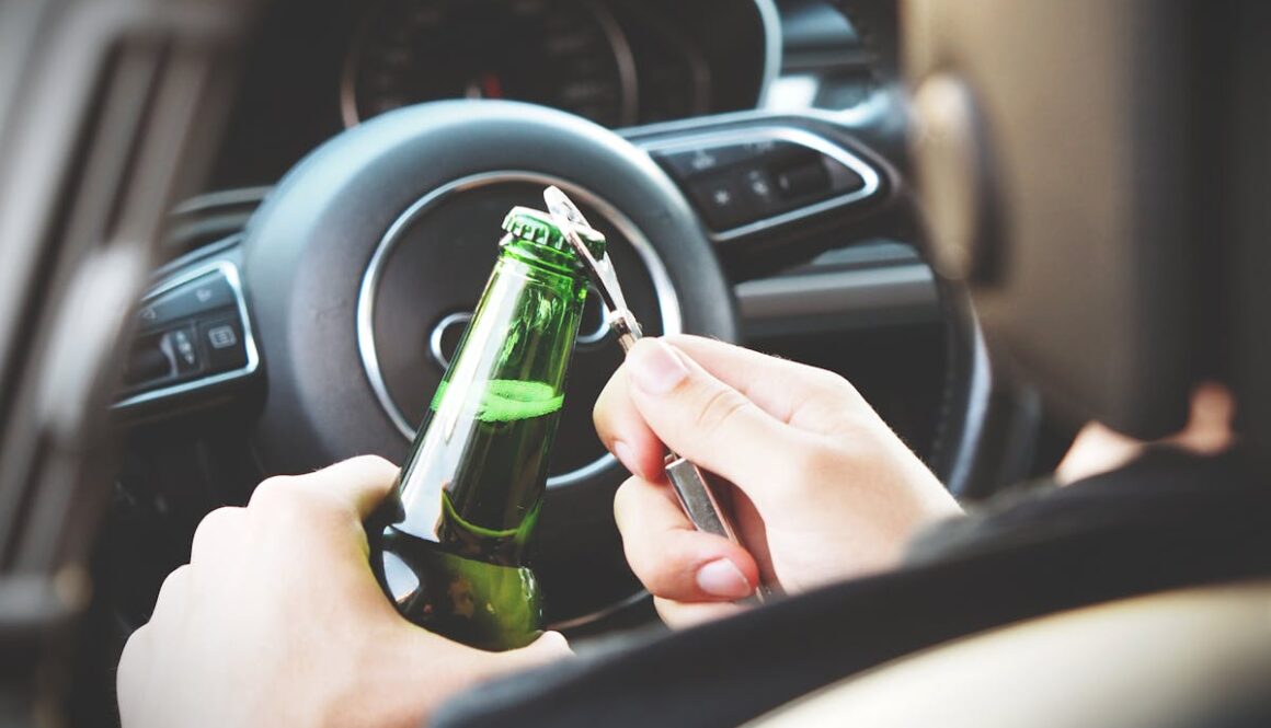 Hands opening a beer bottle inside a car, highlighting the importance of safe driving and awareness of road dangers.