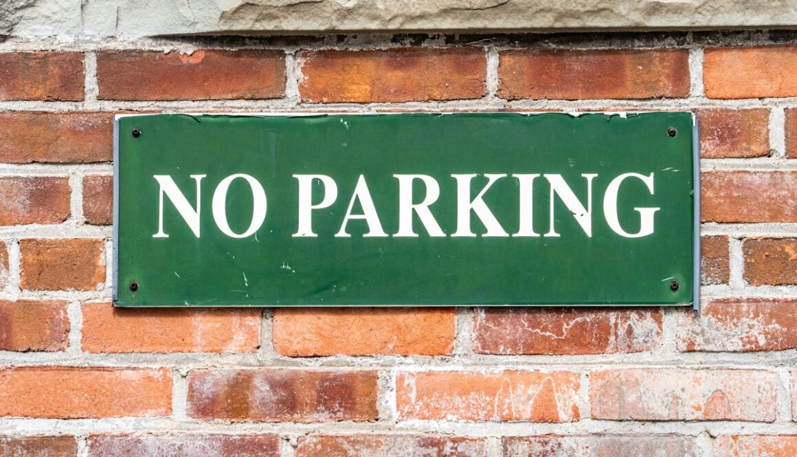 a green sign that says no parking on a brick wall