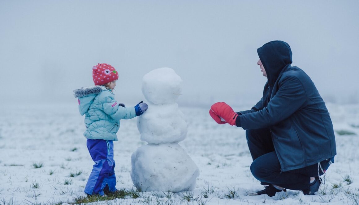 man in black jacket and blue pants sitting on white snow covered ground