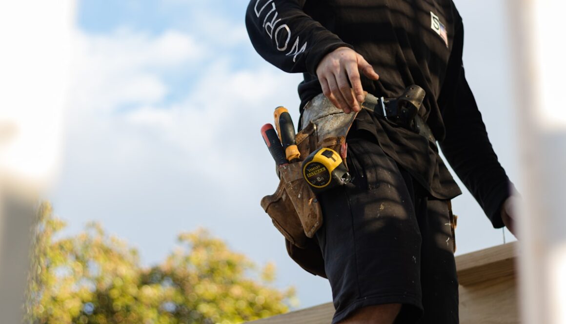 person in black leather jacket holding brown and black hiking shoes