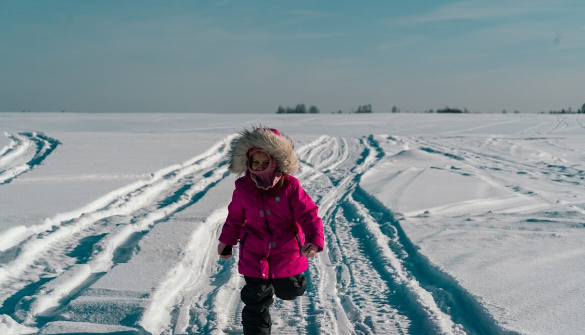 a little girl in a pink coat is walking in the snow