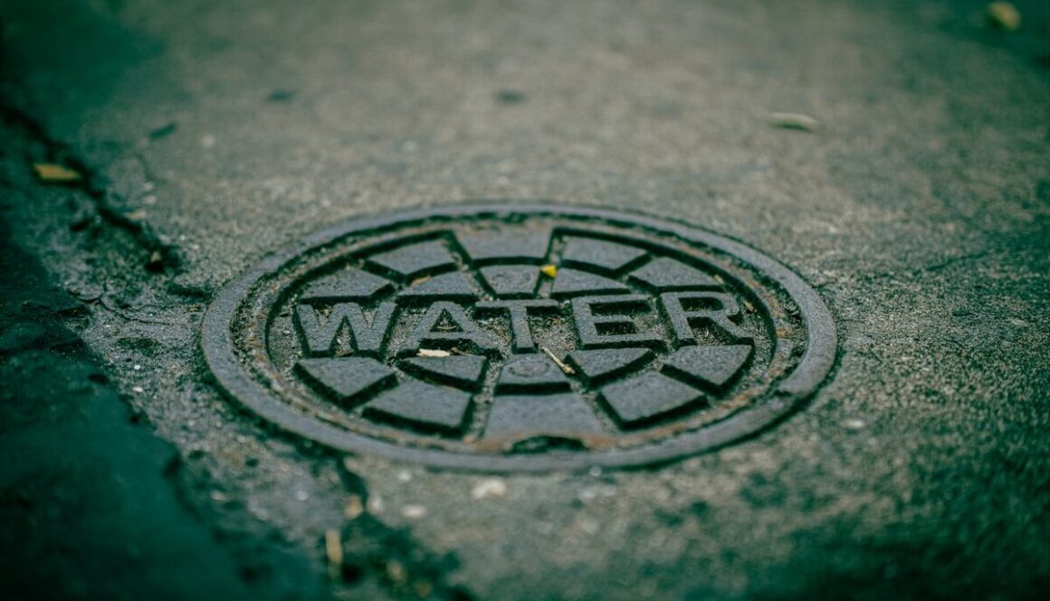 A metal water meter cover on a wet asphalt surface