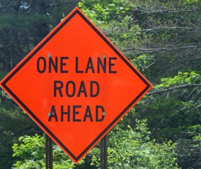 A one lane road ahead sign in front of trees