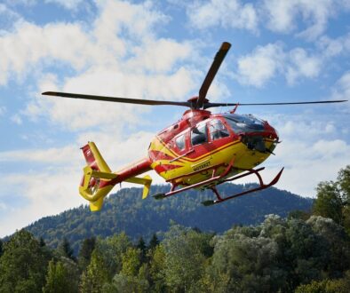 red and yellow helicopter flying over green trees during daytime