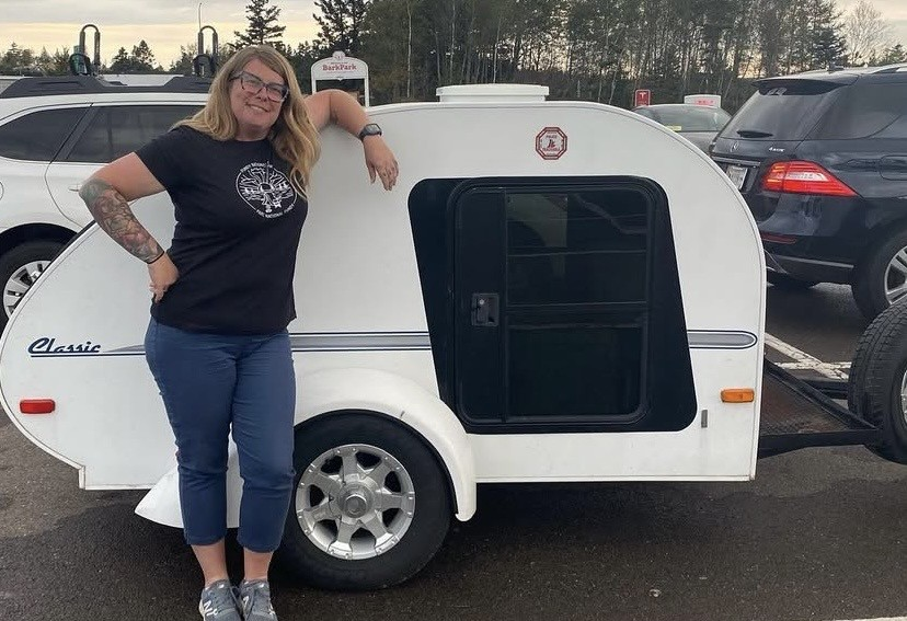 Blonde woman poses next to a trailer 