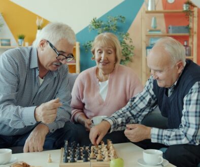 Three seniors playing chess together in a living room.