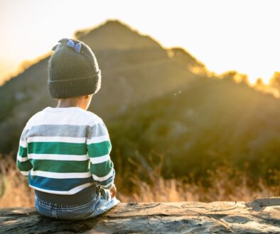 A little boy sitting on a rock looking at the mountains