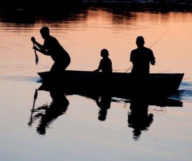 silhouette of three person riding on boat on body of water