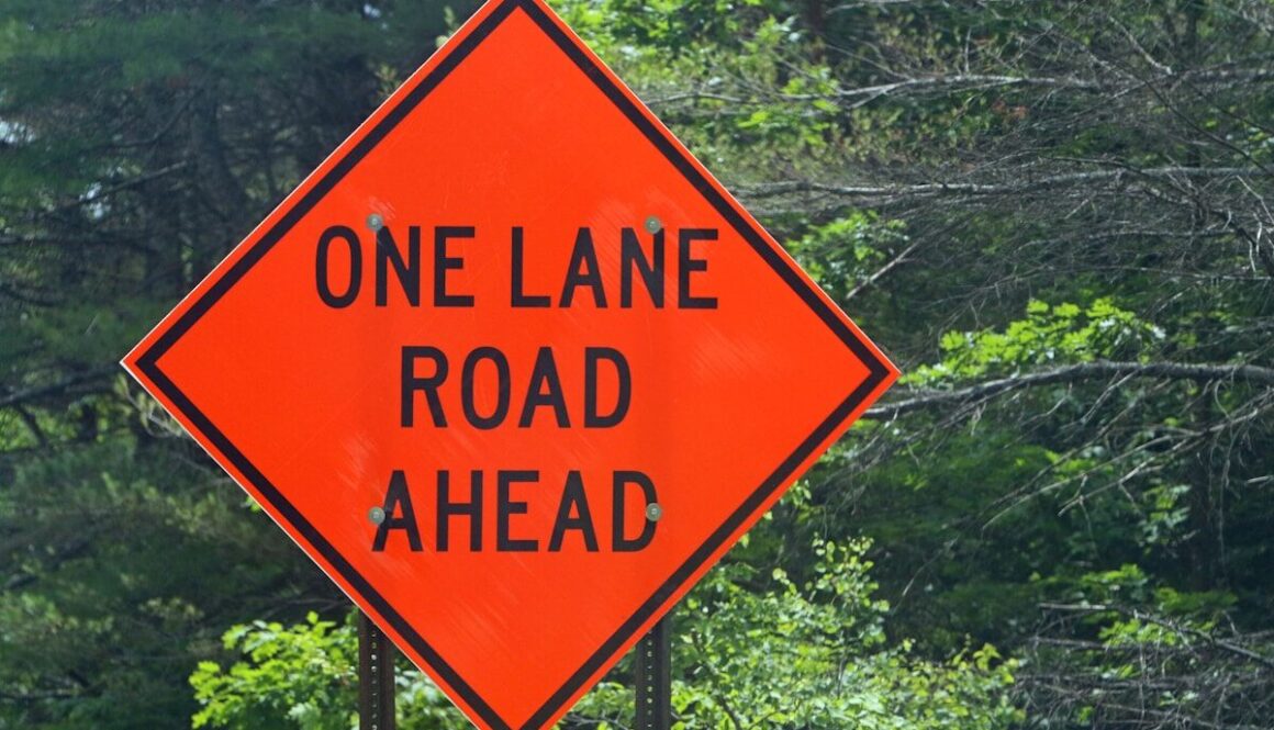 A one lane road ahead sign in front of trees
